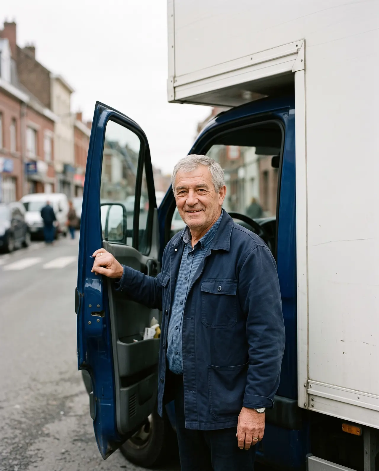 Bernard Moreel, cheveux gris, la main sur la portière ouverte de la cabine bleue d’un camion